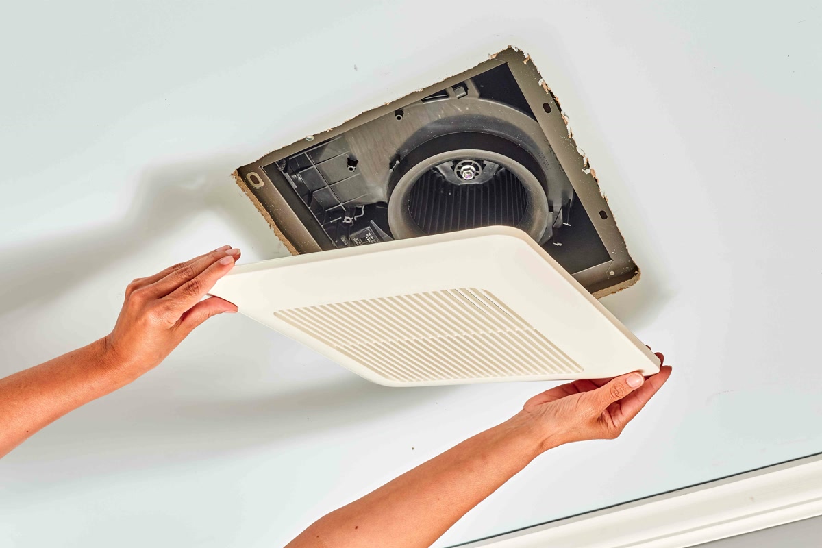 Bathroom exhaust fan being installed in ceiling cutout for automatic humidity-sensing ventilation