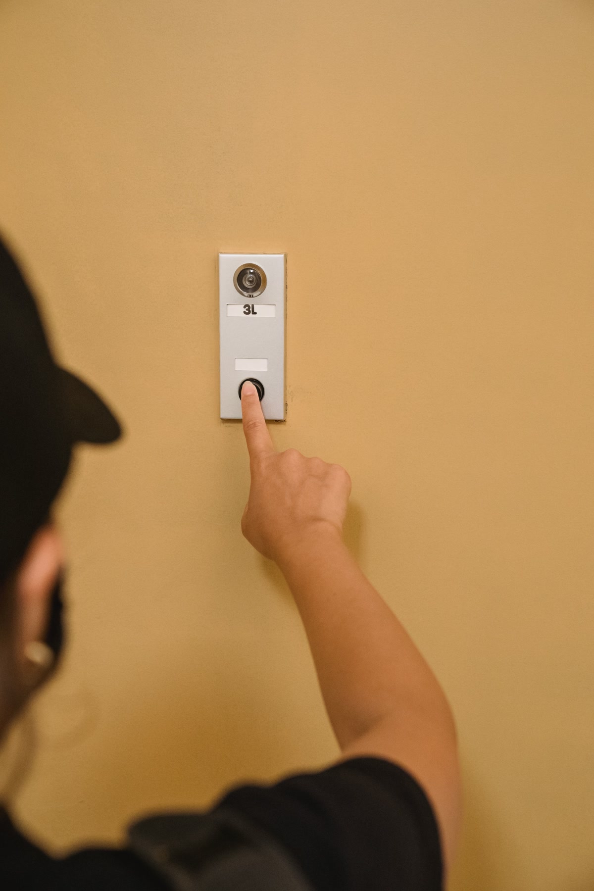 Person pressing a Ring video doorbell on a white door frame